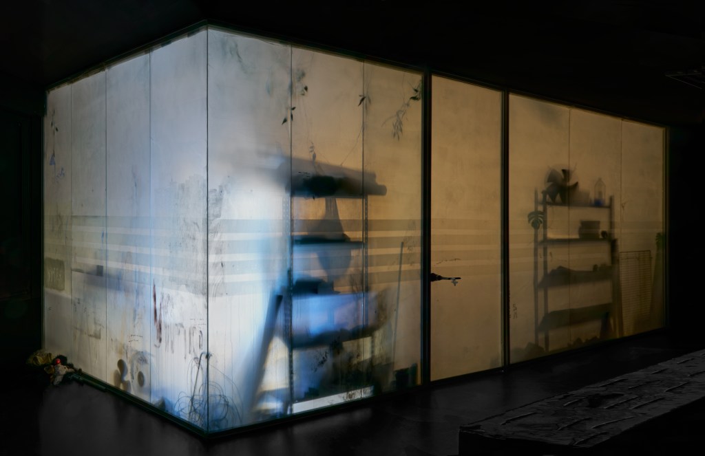 I love seeing myself through the eyes of others (2025), immersive installation featuring sound by Dylan Peirce, plastic, acrylic paint, photographs, found objects, material storage, and light, 614 by 430 by 290 cm. The work constructs a theatrical, layered space charged with personal and collective memory.