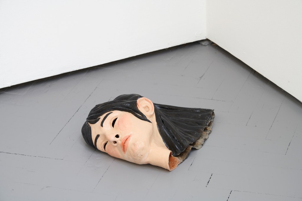 Mask (2025) by Esther Gamsu, made of latex, acrylic paint, and varnish. The piece presents a textured, molded surface suggestive of a theatrical or symbolic facial form.