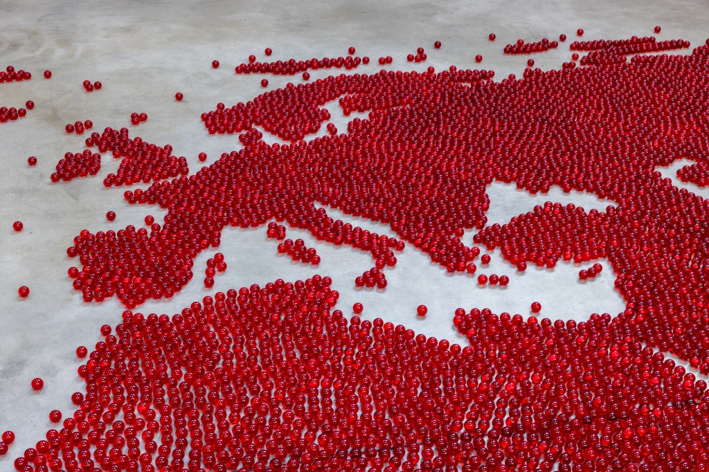 Installation view of Mona Hatoum’s Map (red) (2026), composed of numerous small red glass spheres arranged across the floor to form a map-like configuration