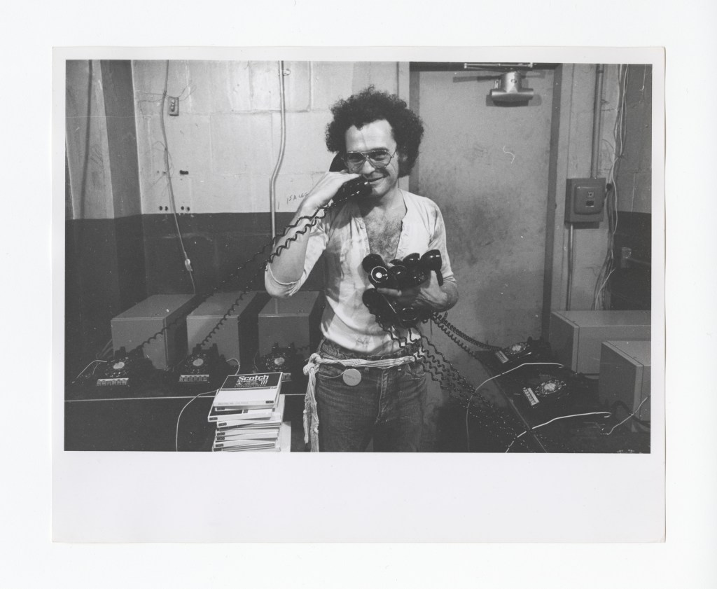 Portrait of John Giorno presenting or interacting with the Dial-A-Poem project, the 1970 telephone-based poetry service.