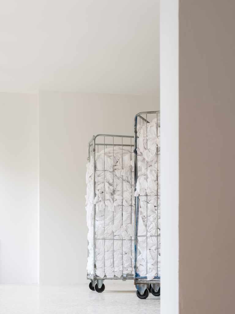 1.3 tons of decommissioned bed linen from 200 Venetian hotels: Large piles or folded stacks of white hotel bed linens fill the installation space, highlighting the scale and material presence of discarded textiles